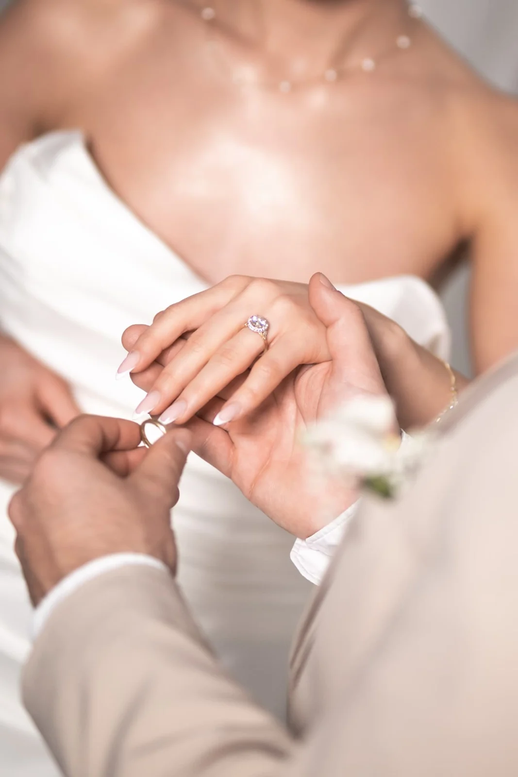 Detailaufnahme beim Anstecken eines Rings vor einem weißen Brautkleid